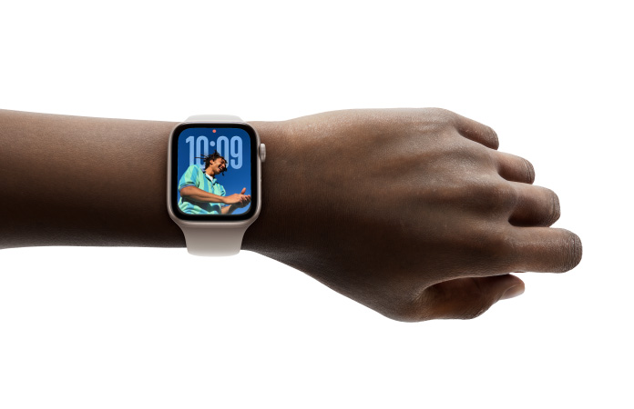 Vue rapprochée d’une Apple Watch argent assortie d’un bracelet en caoutchouc sur un poignet; on y voit l’heure dans le nouveau design avec Liquid Glass