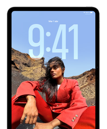 Un iPad muestra la pantalla de bloqueo con números grandes para la hora detrás de la imagen de una persona sentada