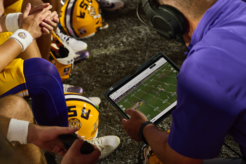 LSU coaching staff and players review footage on iPad Pro on the sideline of a football game.