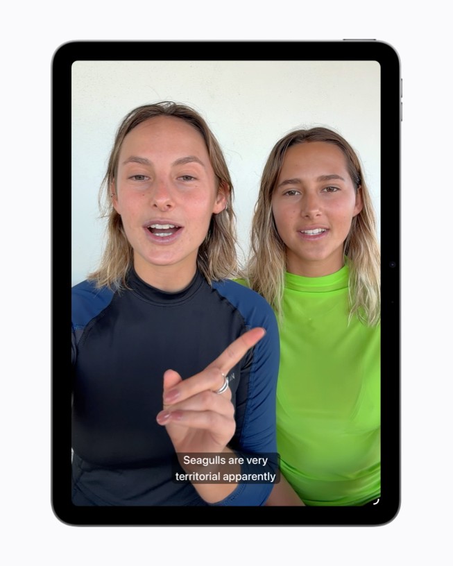 Um quadro de vídeo no iPad mostra duas pessoas conversando, com legendas geradas aparecendo na parte inferior da tela.