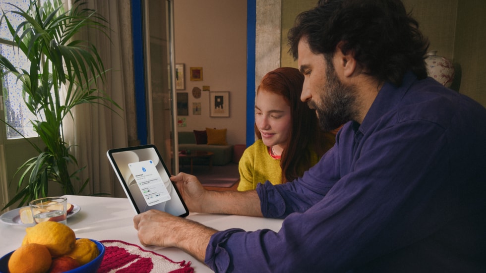 Uma pessoa e uma criança sentadas juntas em uma mesa de madeira, interagindo com o iPad.