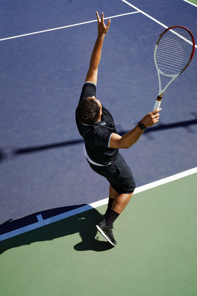 Et foto taget fra oven viser Swupnil Sahai med en ketsjer i hånden, midt i en serv på en tennisbane.