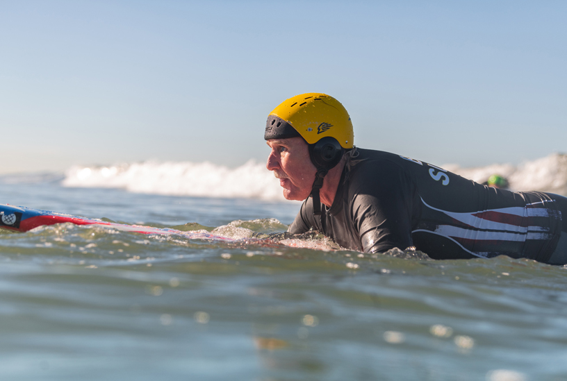 Scott Leason assis sur sa planche dans l’eau.