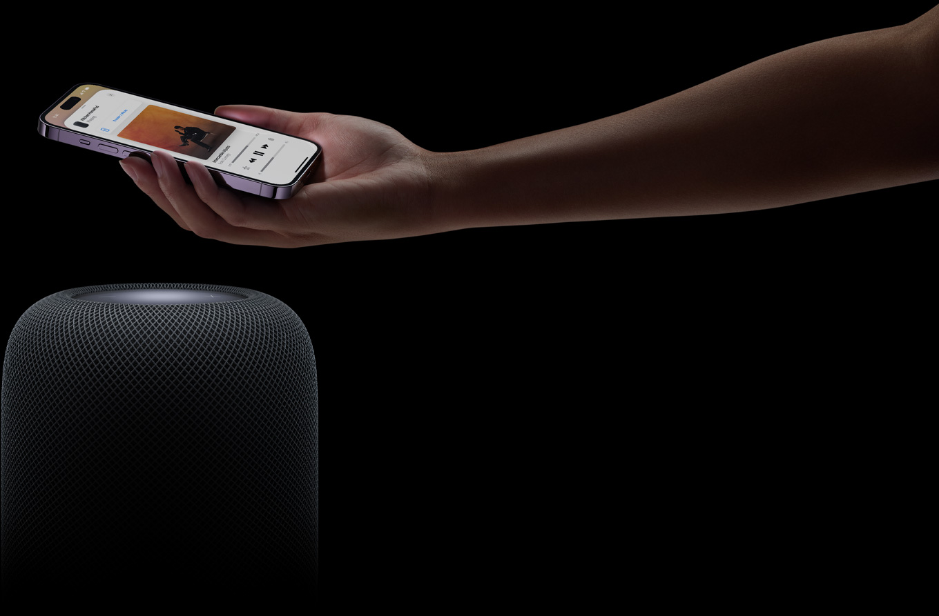 En hand kommer in från höger på sidan och håller en iPhone ovanför en HomePod-högtalare