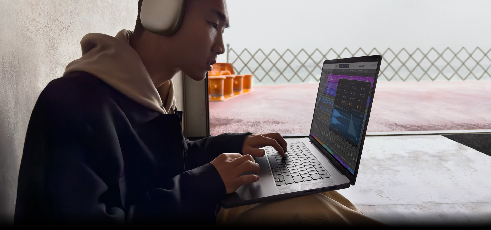 มุมมองด้านข้างของบุคคลหนึ่งที่สวม AirPods Max ขณะใช้ Logic Pro บน MacBook Pro รุ่น 16 นิ้ว, หน้าจอแสดงพื้นที่ทำงานของ Logic Pro